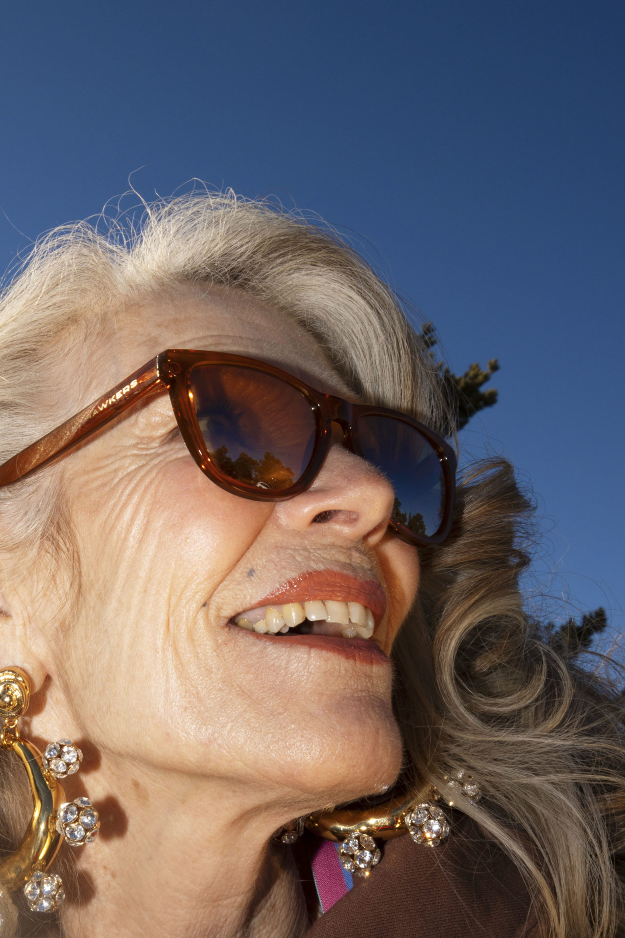 Portrait d'une femme agée aux cheveux blanc avec des lunettes de soleil et de grande boucle d'oreille 