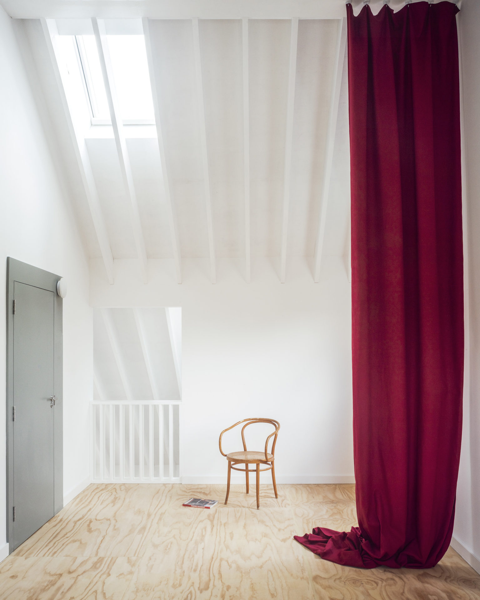 Photographie d'une chaise dans un intérieur blanc avec un rideau rouge en premier plan