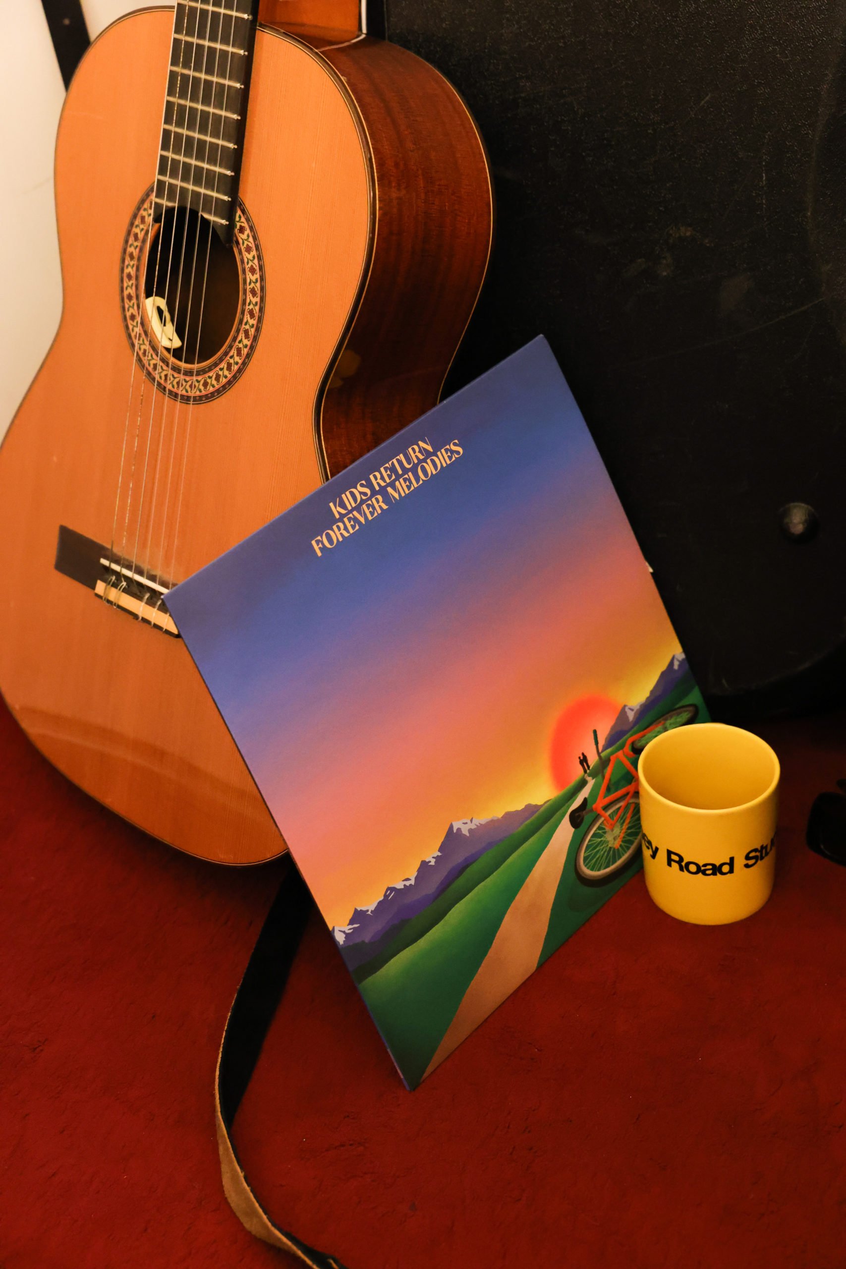 Le vinyle des Kids Return est posé sur une guitare sèche à côté d'ue tasse jaune abbey road.