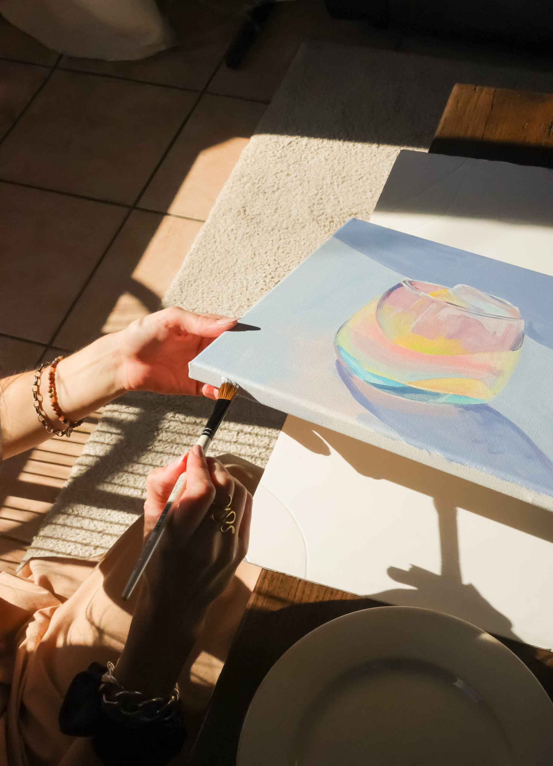 La main de Morgane Clavaud en train de finir une toile représentant un verre sur un fond bleu