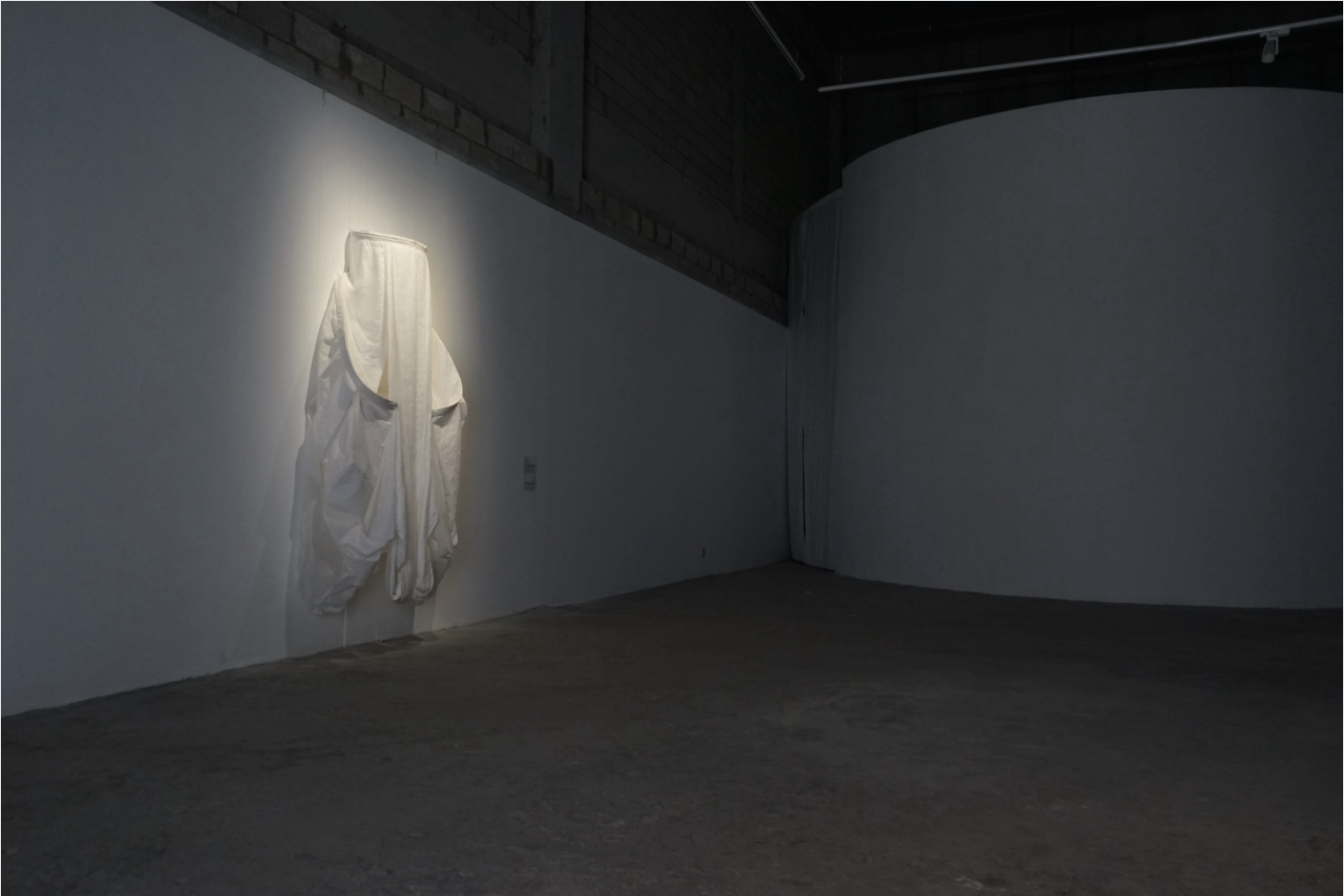 Oeuvre de Filwa Nazer de son exposition In the fold. Tissu clair suspendu dans une salle sombre